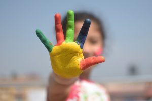 child's hand with different colours painted on each finger and the palm